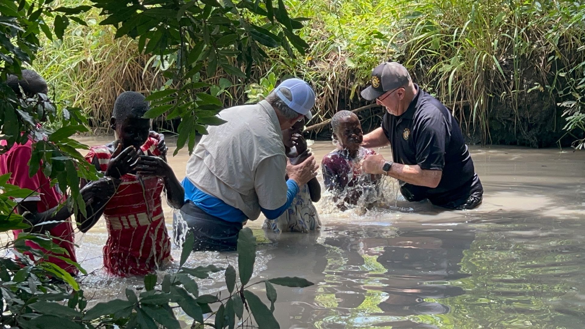 A group of people are being baptised in a river.