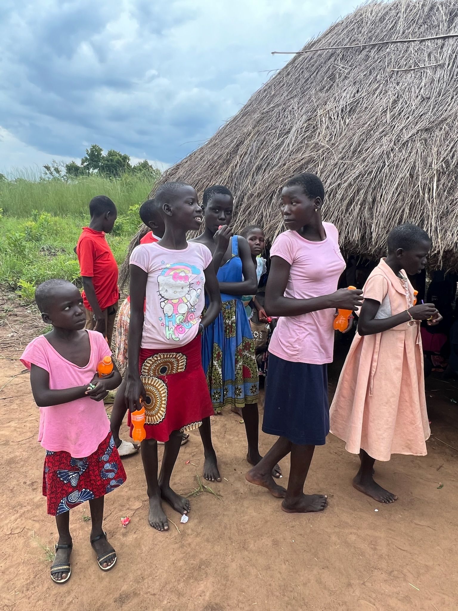 A group of young girls are standing in front of a thatched roof.