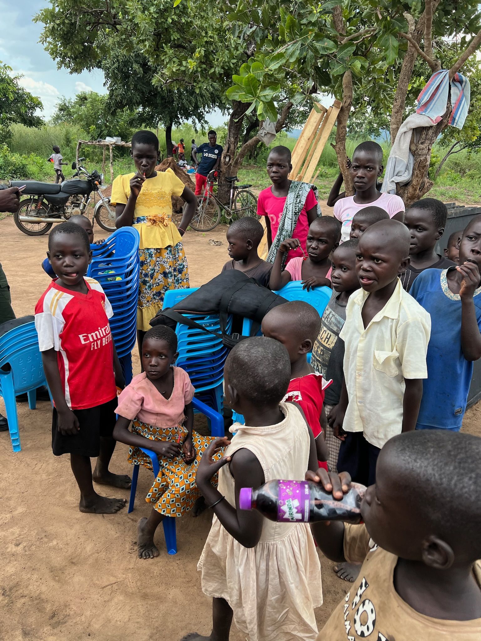 A group of children are standing in a dirt field.