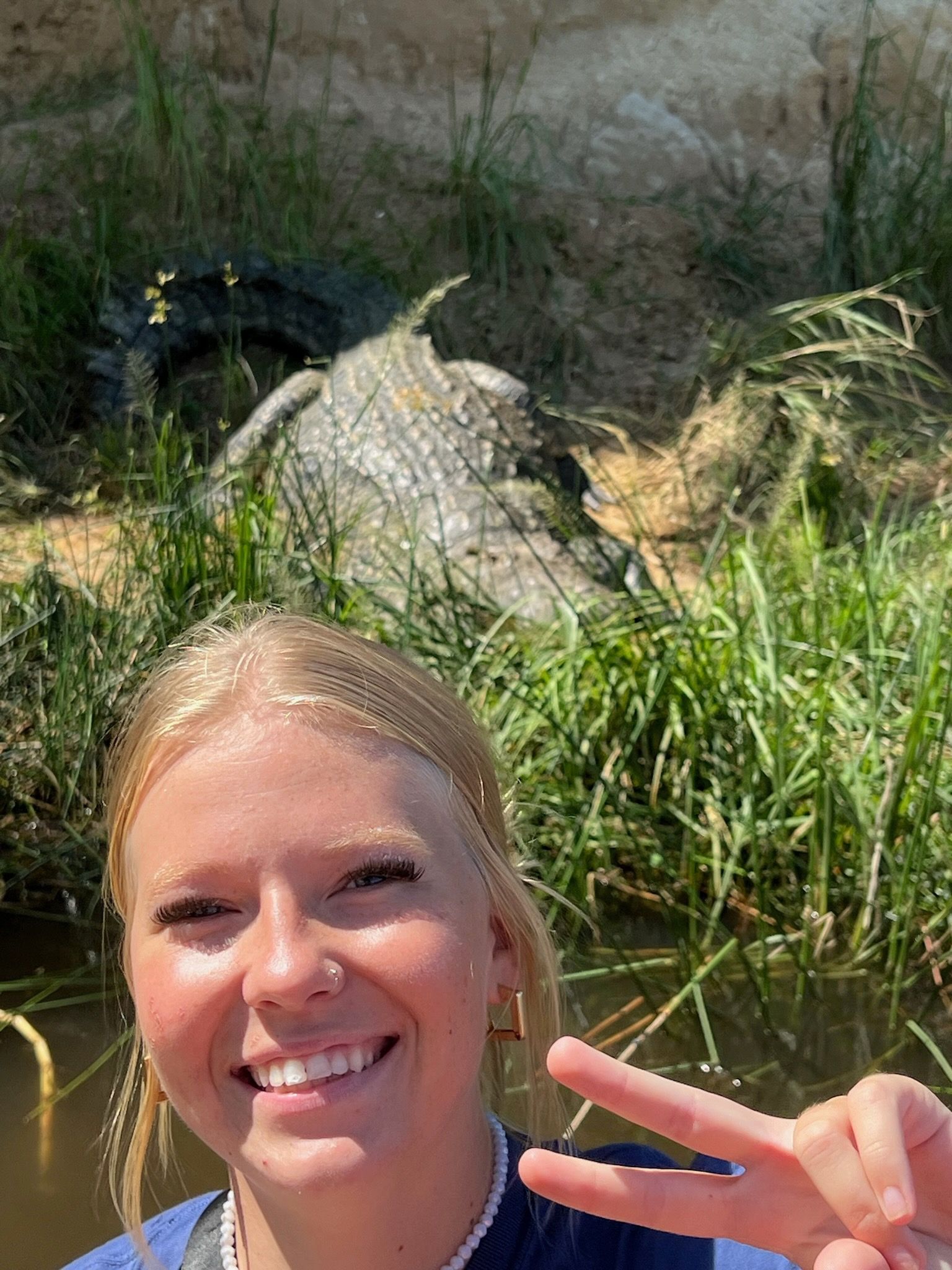 A woman is smiling and giving a peace sign in front of an alligator.