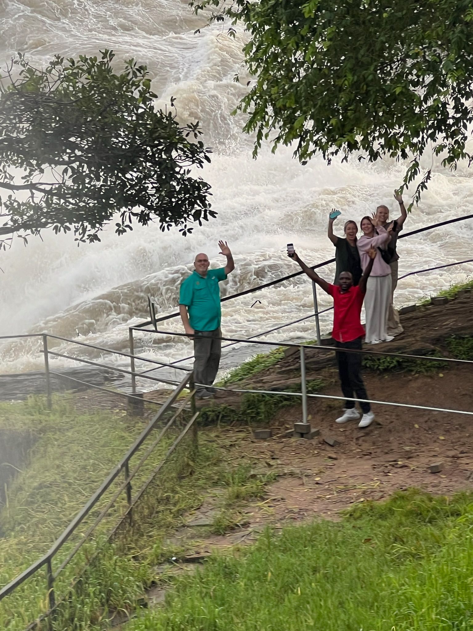 A group of people are standing on a fence looking at a waterfall.