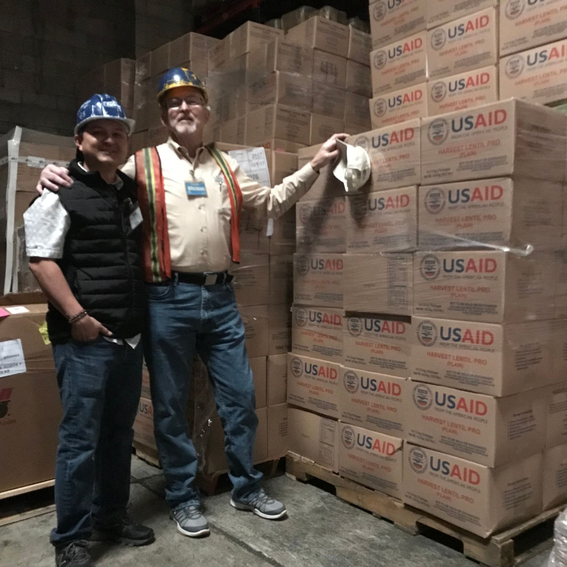Warehouse stacked with USAID Harvest Lentil Pro boxes connected to Amigos Internacionales food distribution records