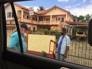 Two men are standing in front of a large house talking to each other.