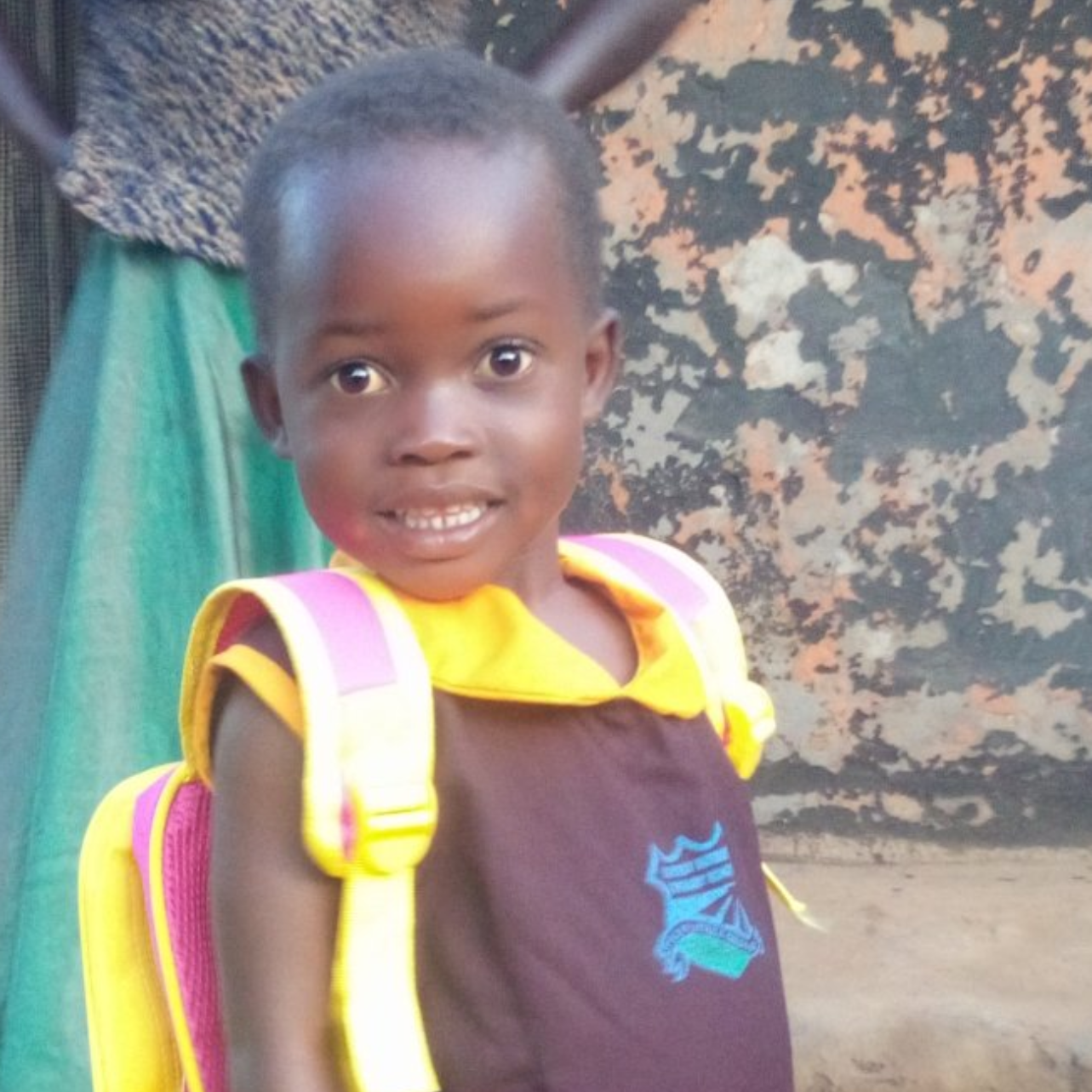 Young child with a backpack smiles at the camera, wearing a school uniform.