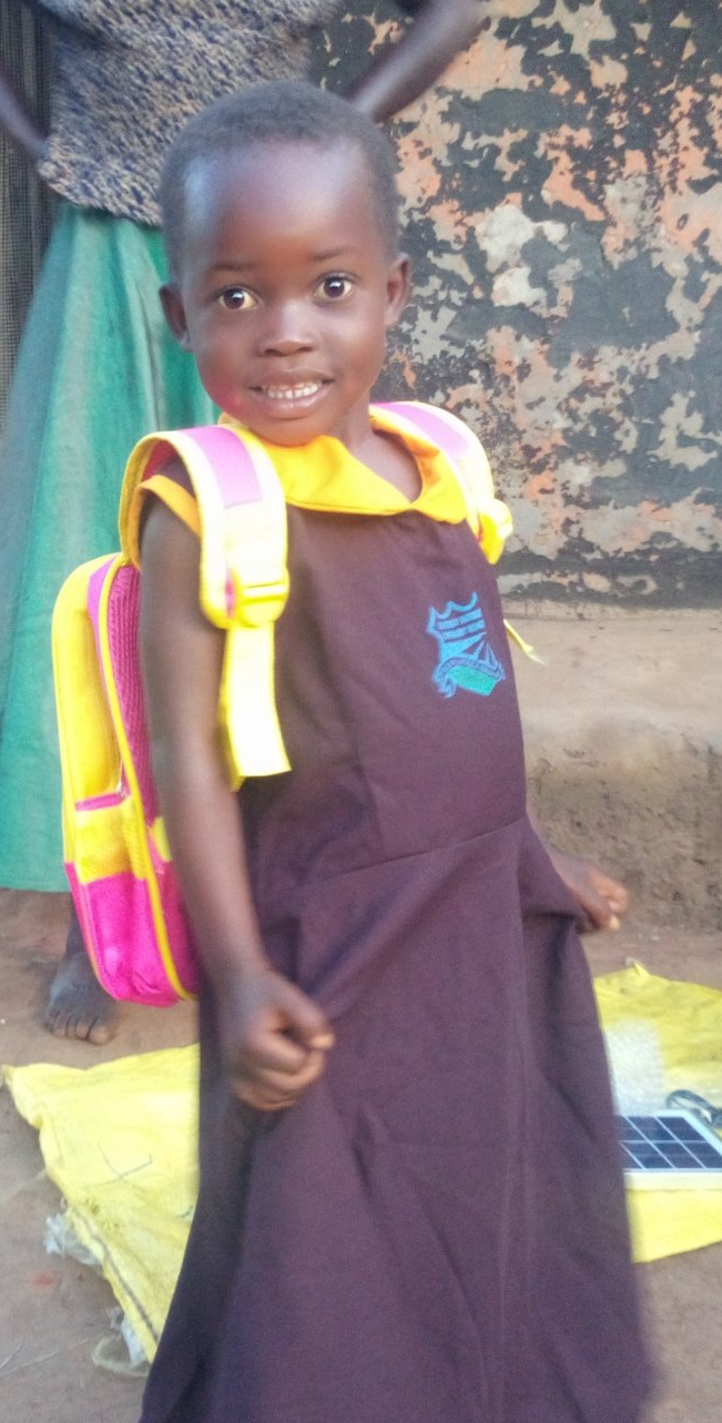 Young girl in school uniform with backpack smiles outside.