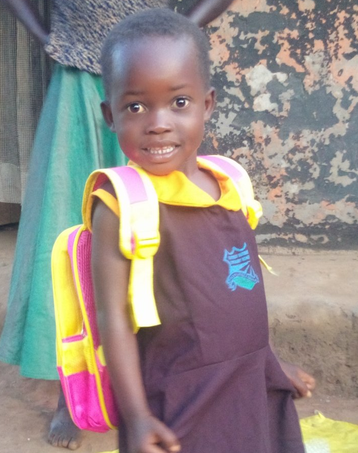 Young child wearing a dark dress and backpack smiles, standing near a solar panel and radio.