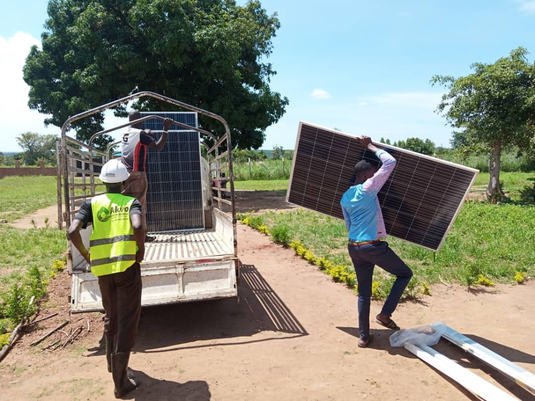 A man is carrying a large solar panel in front of a truck.