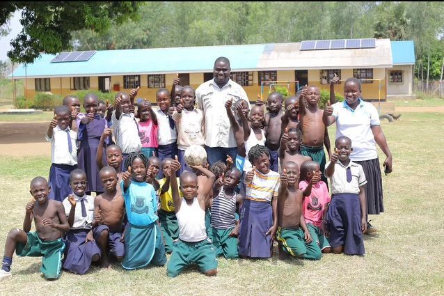 Group of school children and two adults outside a building with solar panels.