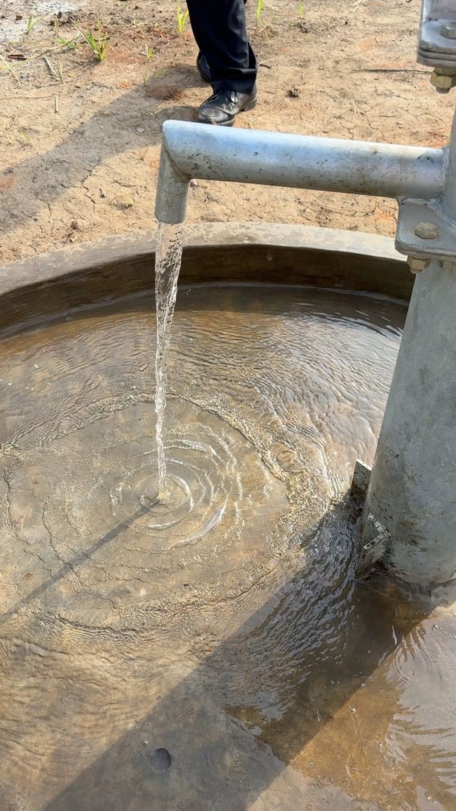 Water flows from a metal spout into a concrete basin, a person's legs visible in the background.