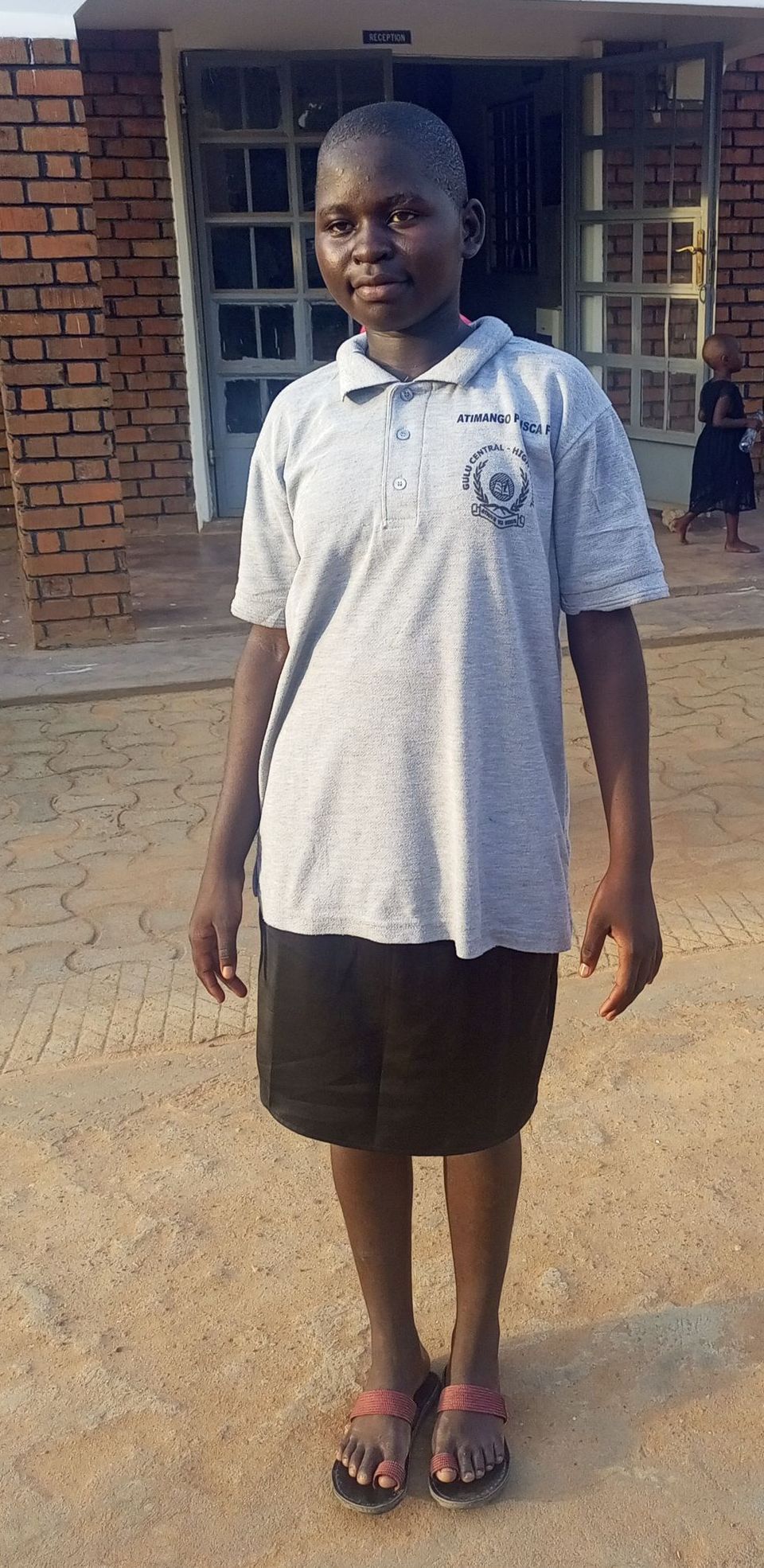 A person wearing a grey shirt and black skirt stands in front of a brick building.
