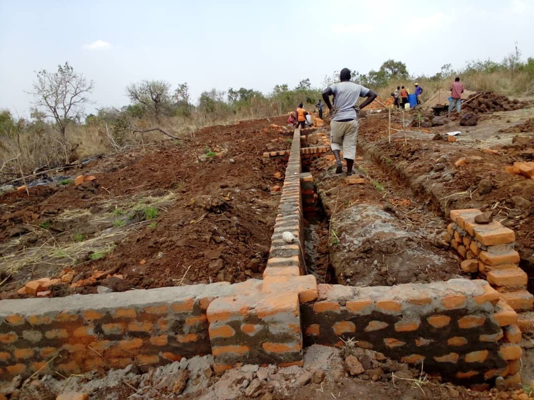 Construction workers building a brick structure on a hillside, using red bricks and mortar, outdoors.