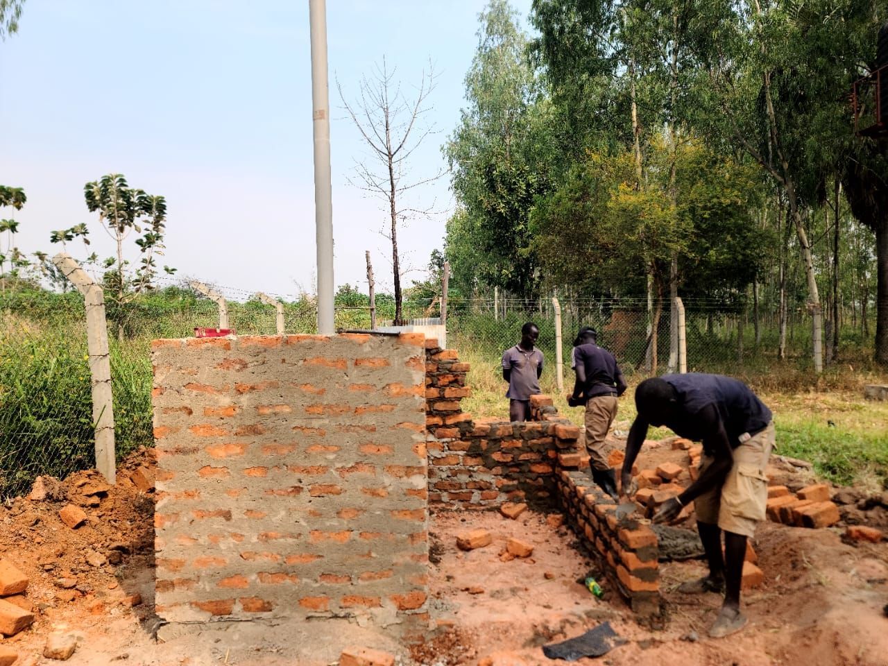 A group of men are working on a brick wall in a field.