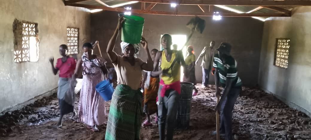 People inside a building, some carrying buckets. The floor is muddy. Windows are visible on walls.