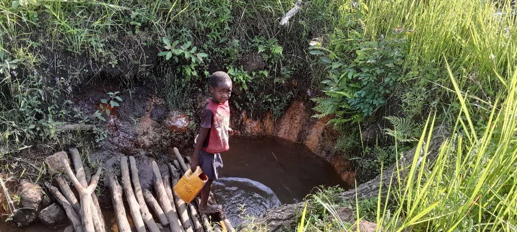 A young boy is standing next to a river holding a bucket of water.