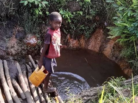 Young boy getting water from a dirty water hole