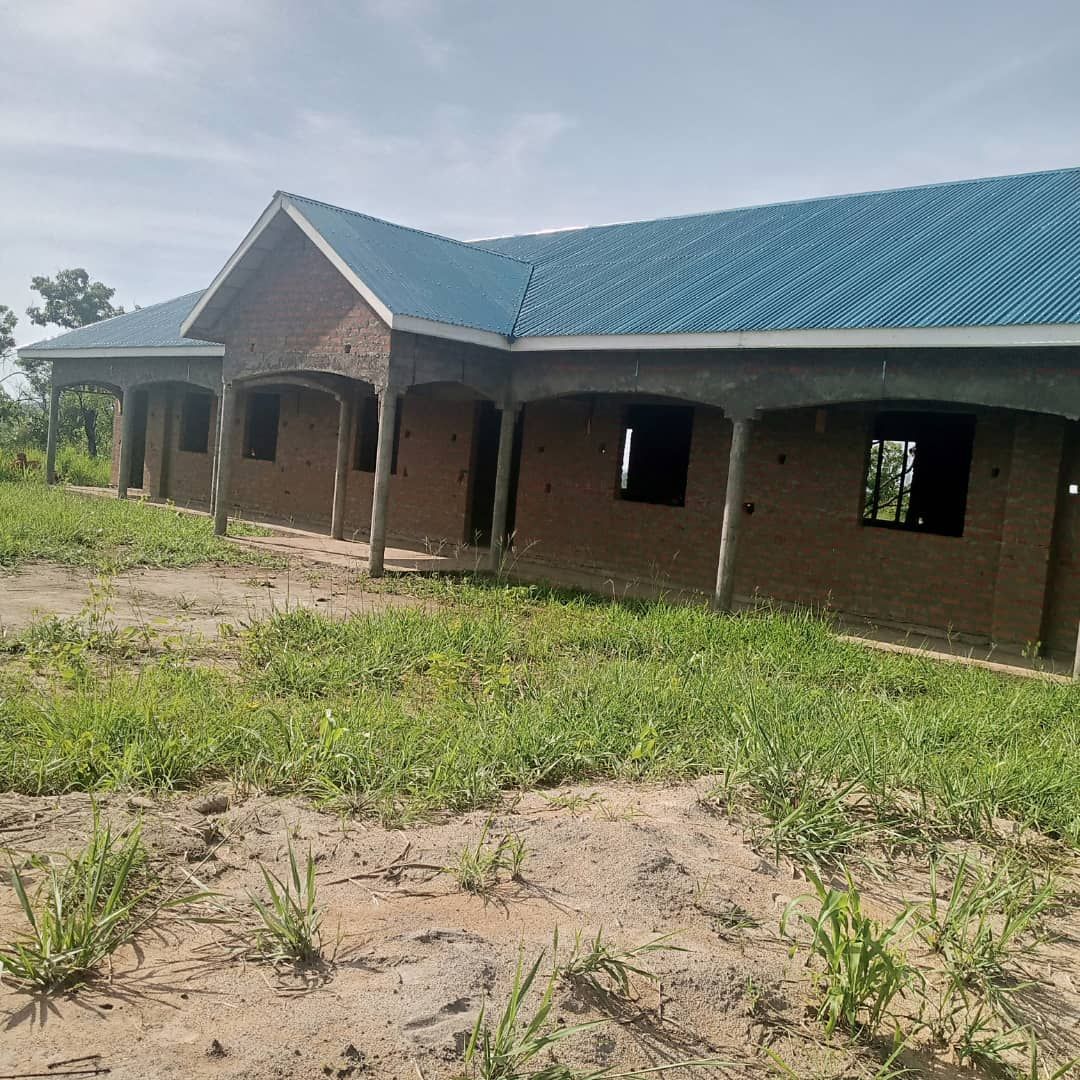 A brick house with a blue roof is sitting in the middle of a grassy field.