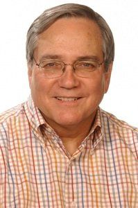 A man wearing glasses and a plaid shirt smiles for the camera