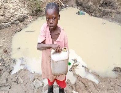 a young boy is standing in the mud holding a can .