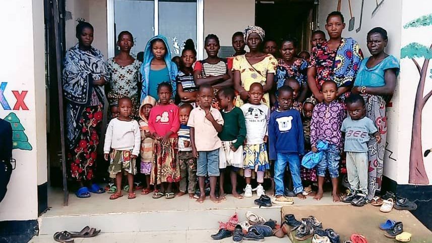 Group of children and adults posing in front of a building with colorful painted walls.