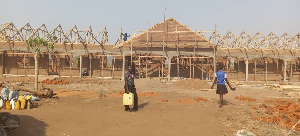 Two people are standing in front of a Bupong School building under construction.