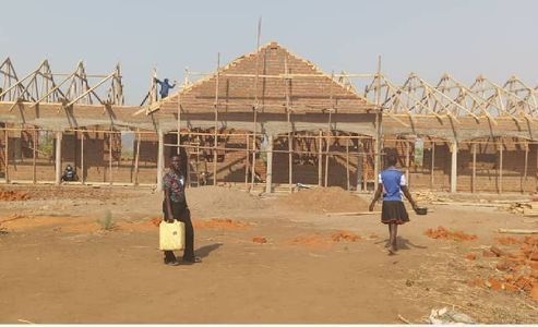 Construction site: wooden frame building with thatched roof; two children walk past with a water jug.