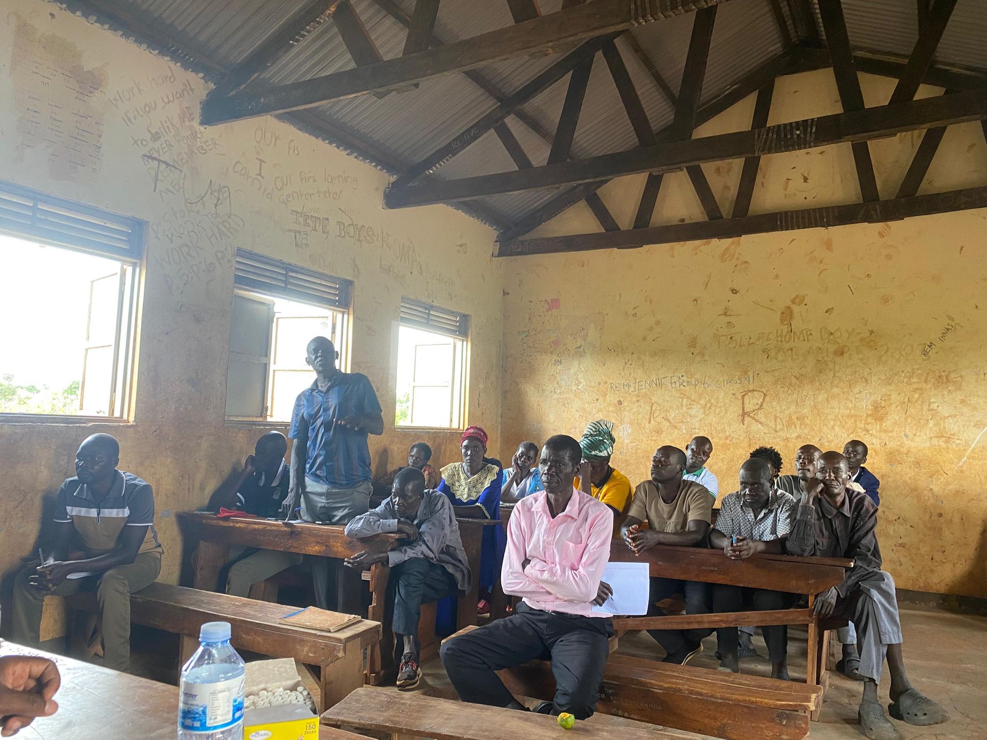 Amigos leadership meeting with village elders and community members inside a Nwoya classroom, June 2026.