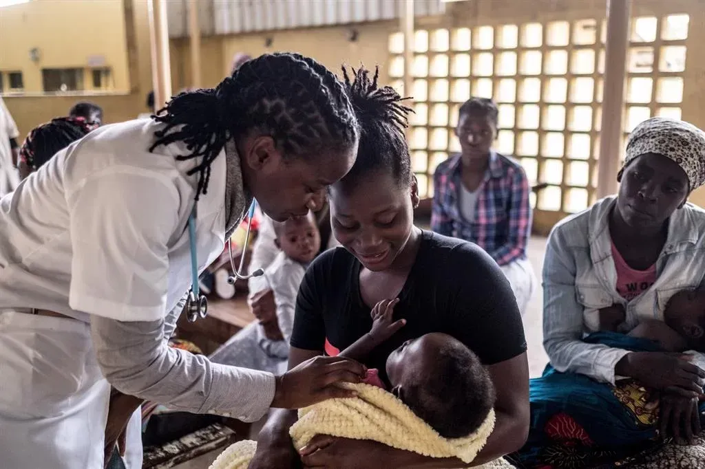 A woman is holding a baby in her arms while a doctor examines it.