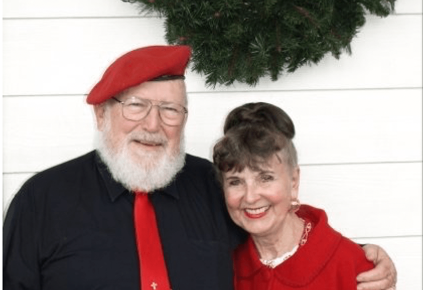 A man and woman are posing for a picture in front of a wreath.