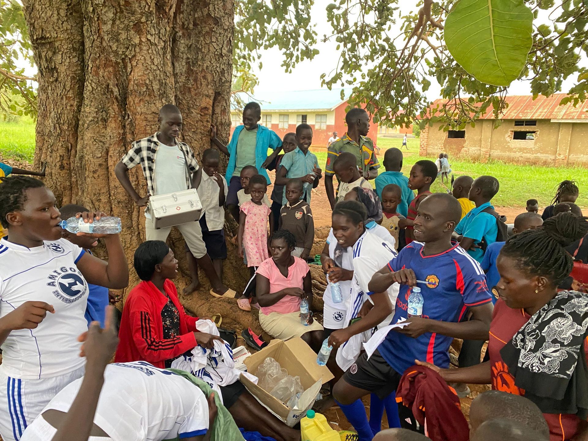 A group of people are sitting under a tree drinking water.