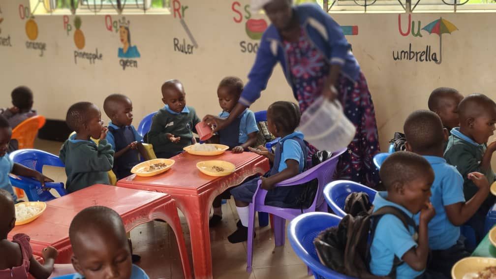 A group of children are sitting at tables and a woman is pouring water into their cups