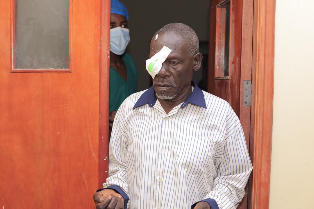 Man with eye patch exiting doorway; a person in a mask and scrubs stands behind him.