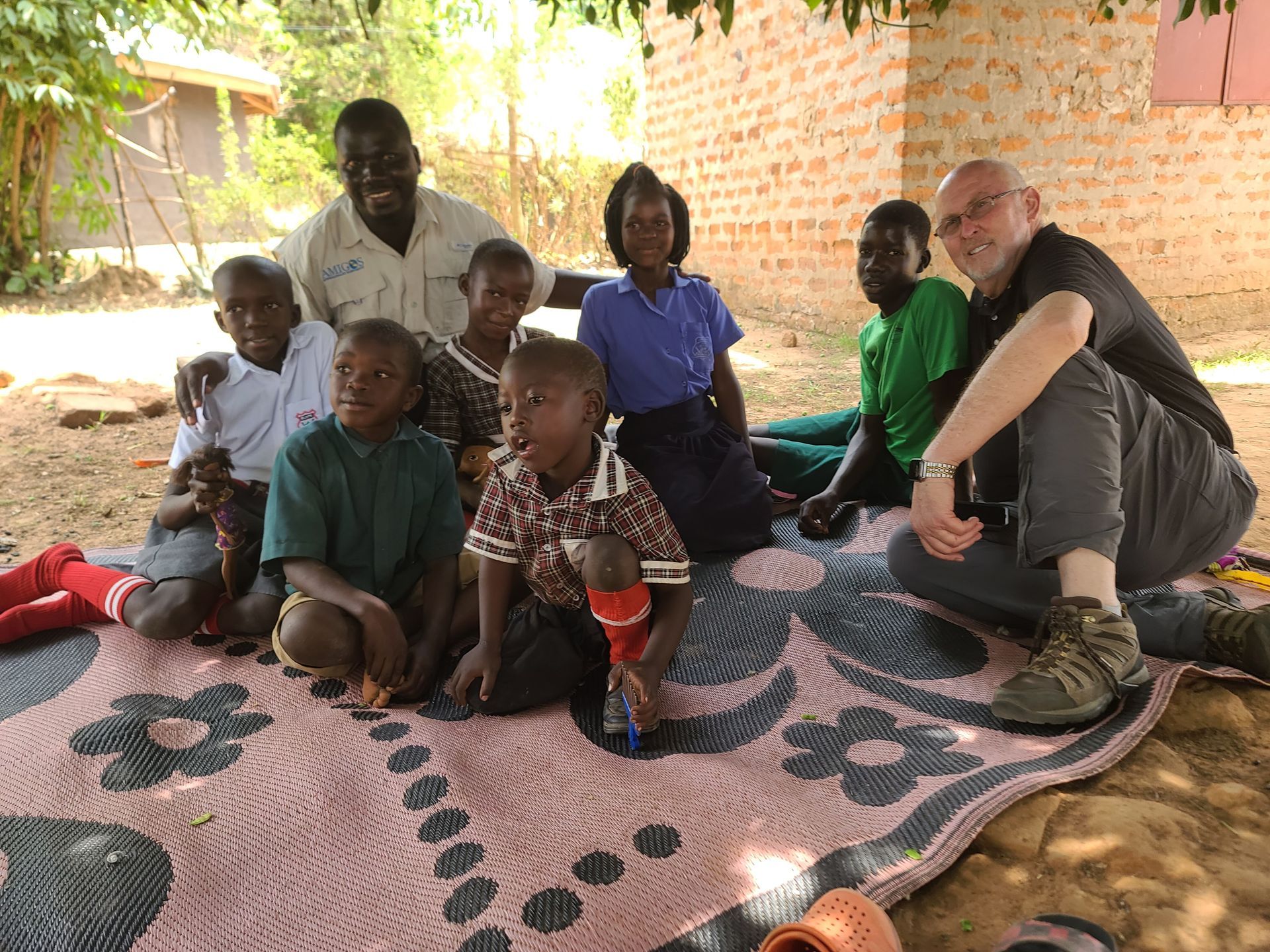 A group of people are sitting on a blanket in the dirt.