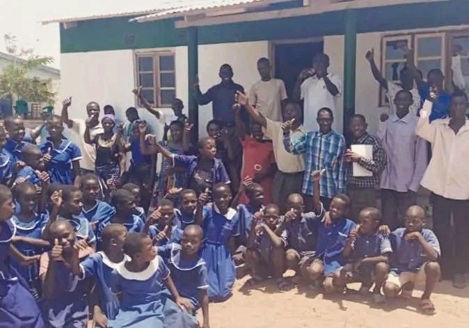 Group of Malawian African schoolchildren and adults cheering in front of a school building.
