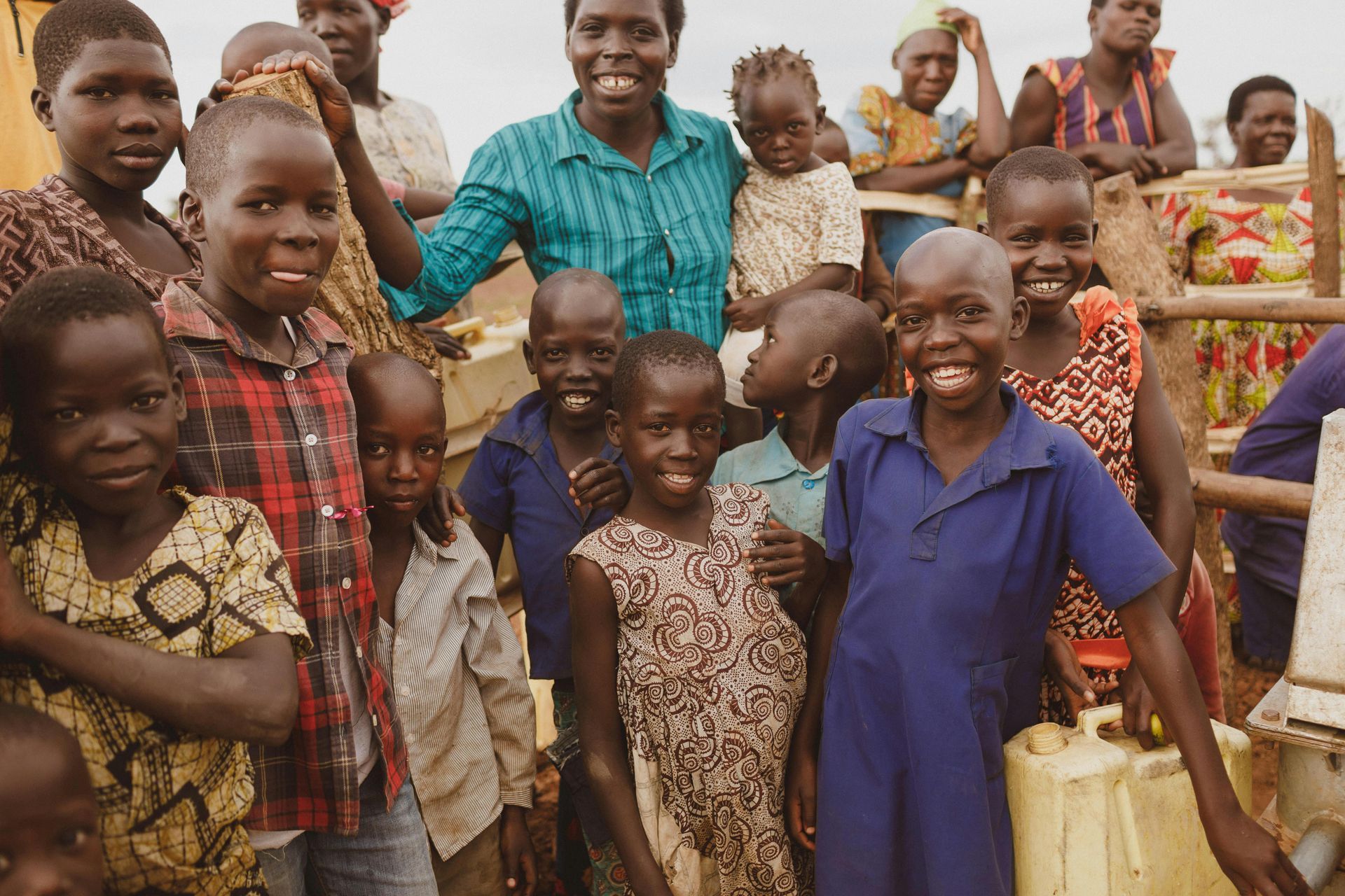 A group of children are posing for a picture with a woman in the background.