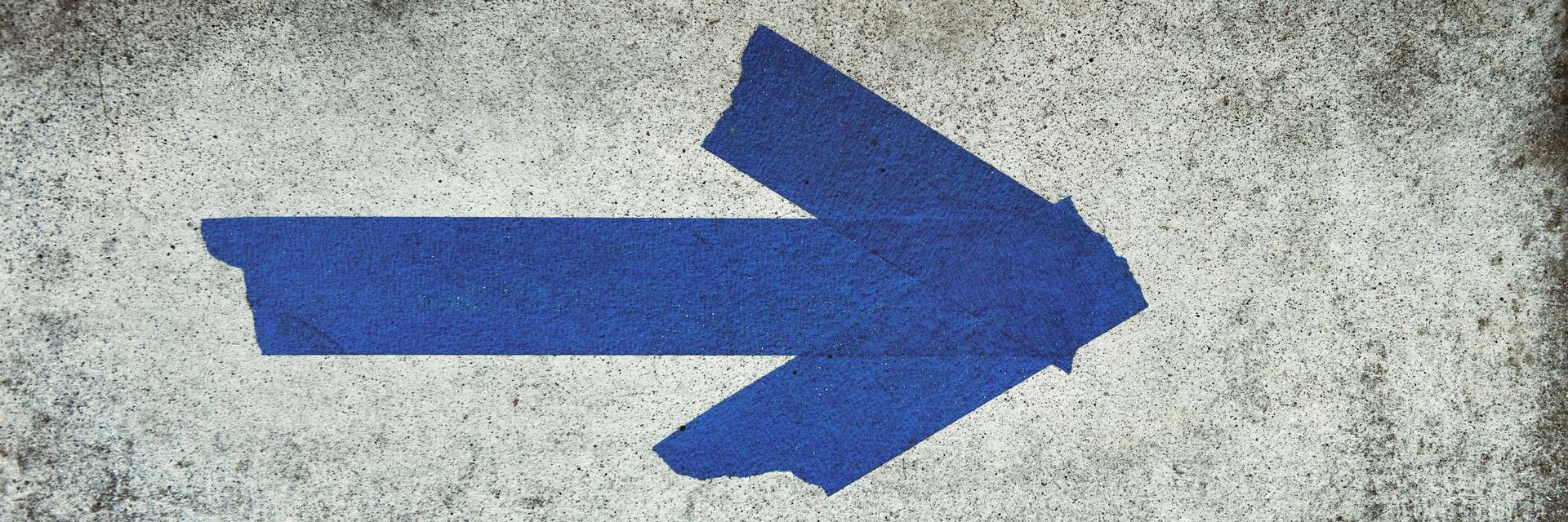 A blue arrow is painted on a white surface.