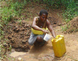 Lucy, crouches beside a muddy puddle, pouring water from a plastic bag into a yellow jerrycan.