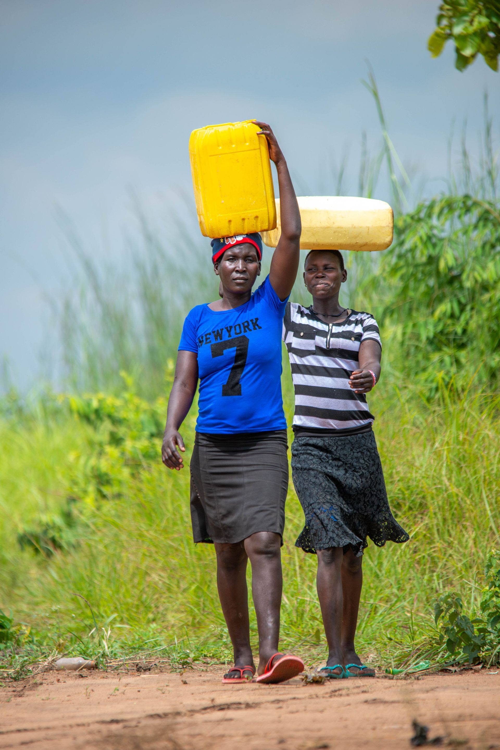 Two women are carrying buckets of water on their heads.