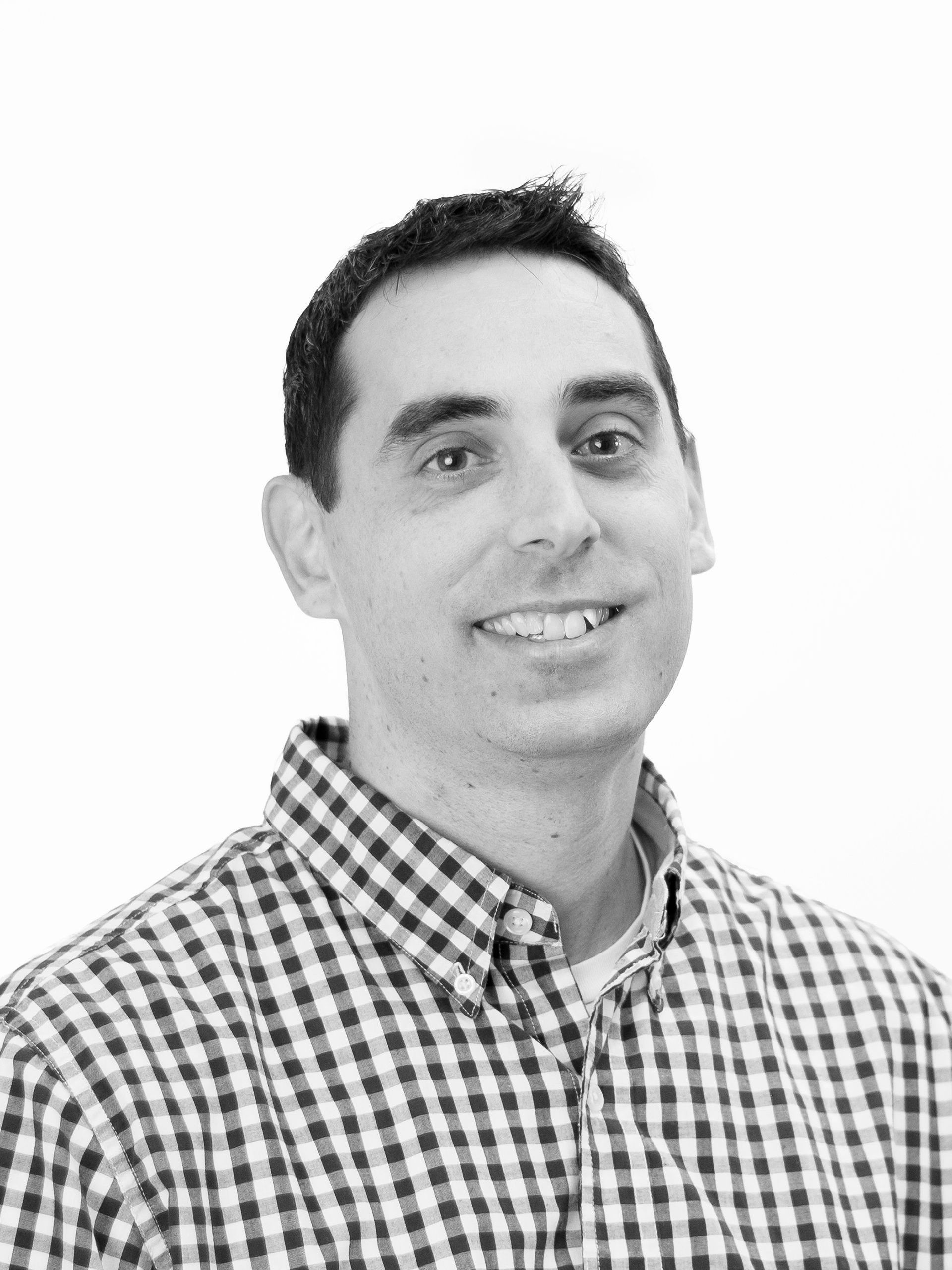 A man in a plaid shirt is smiling in a black and white photo.