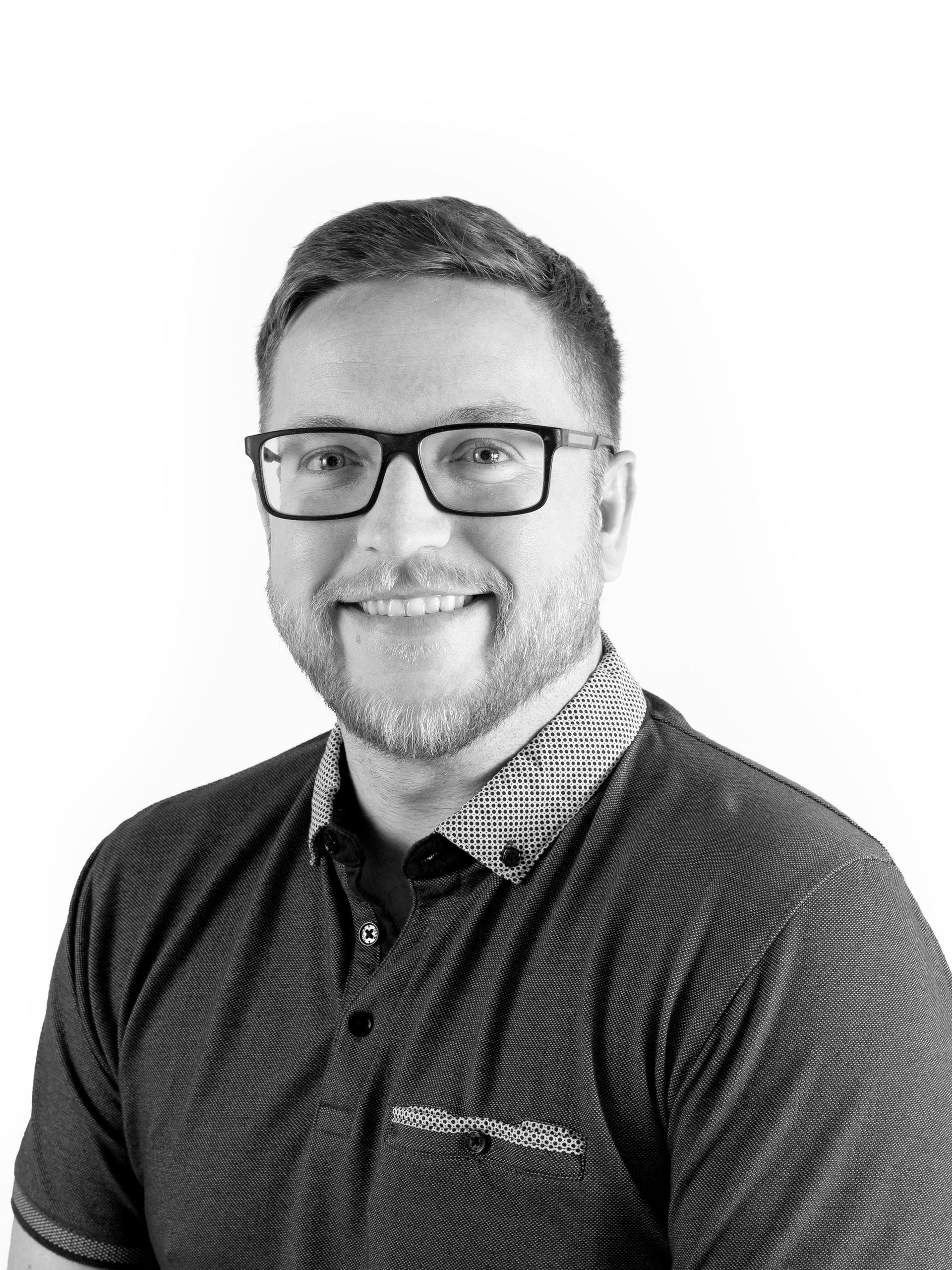 A man wearing glasses and a polo shirt is smiling in a black and white photo.