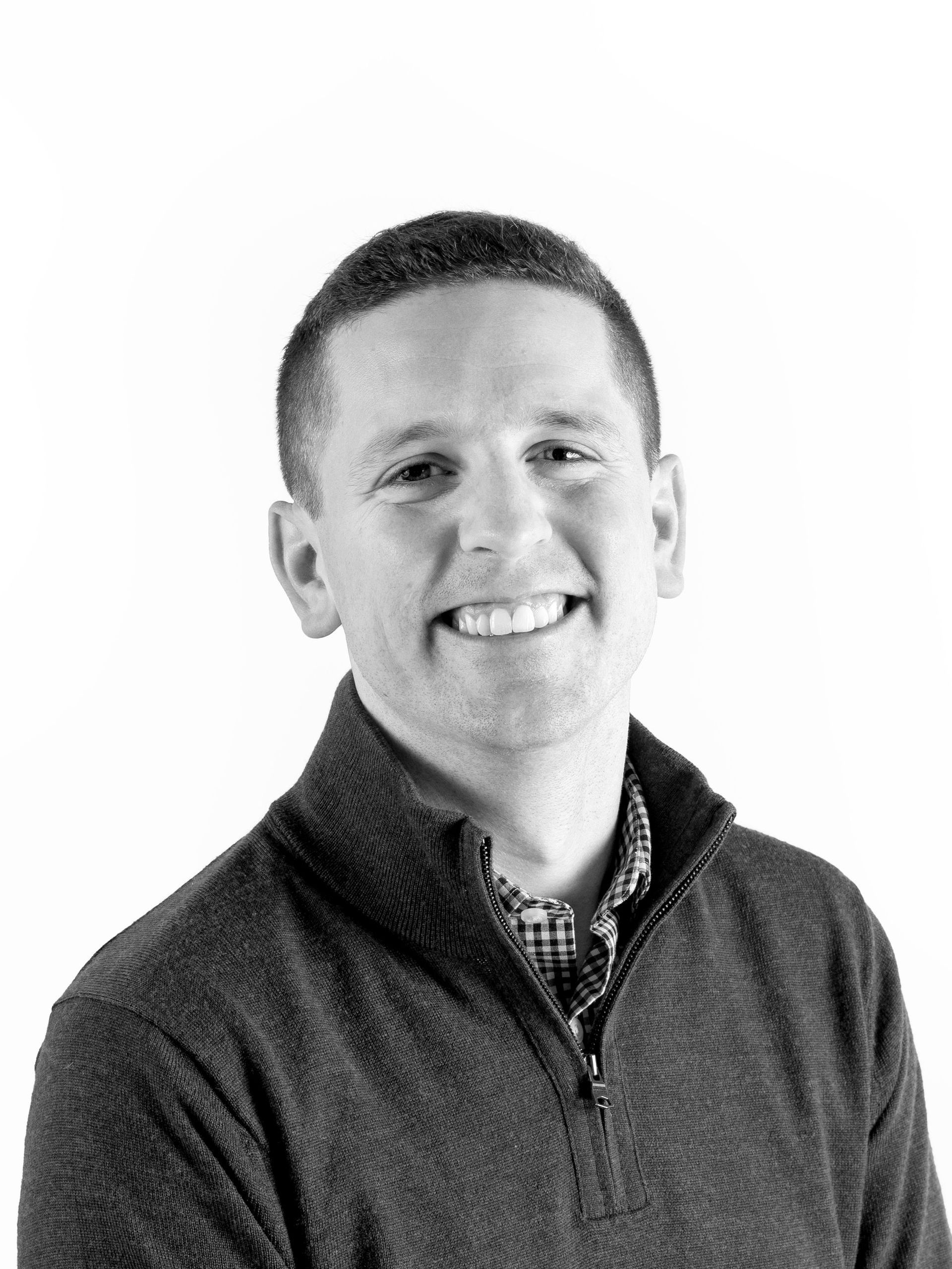 A man in a sweater is smiling in a black and white photo.
