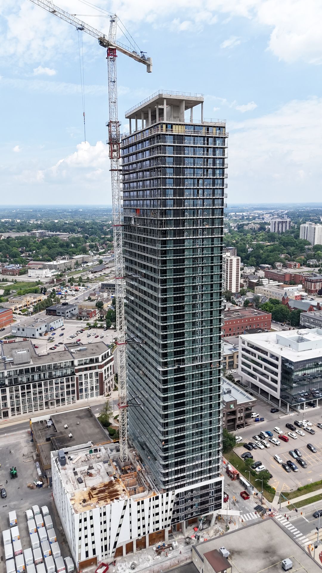 Tall skyscraper under construction, crane on top, surrounded by city buildings and blue sky.