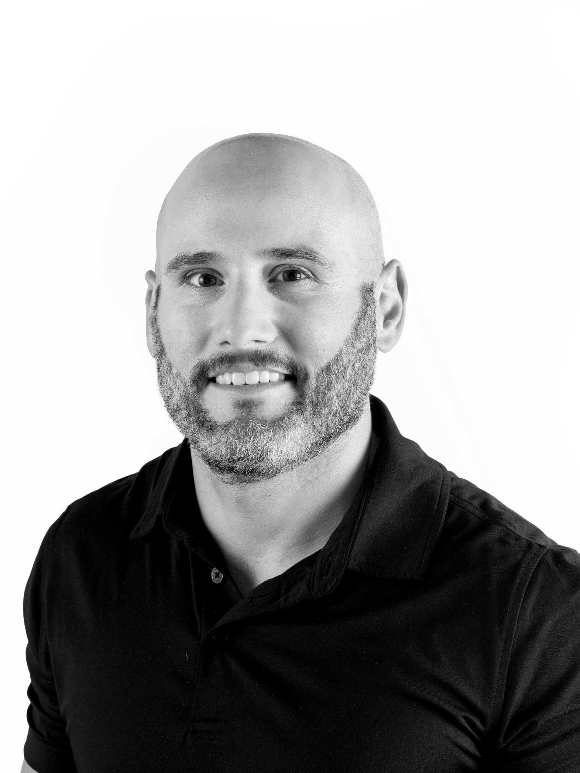A bald man with a beard is smiling in a black and white photo.