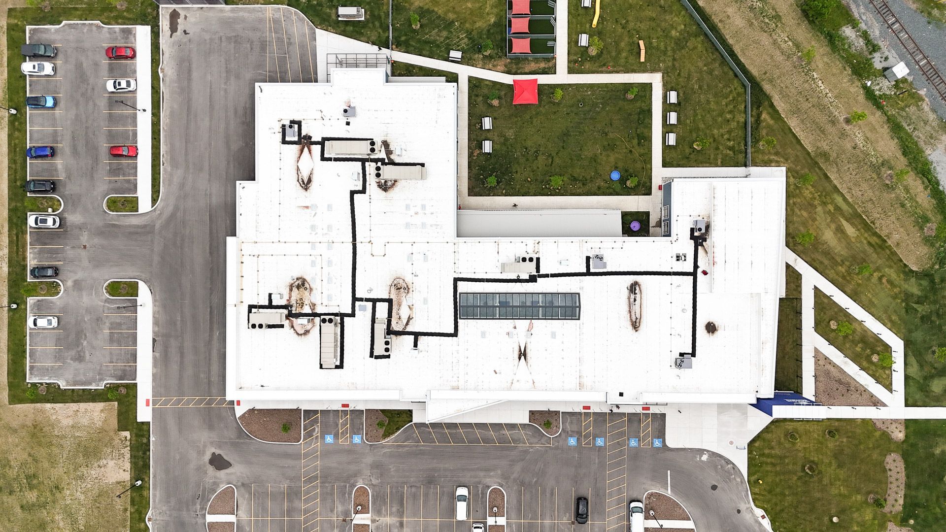Overhead view of a white commercial building with a rooftop garden and parking lot.