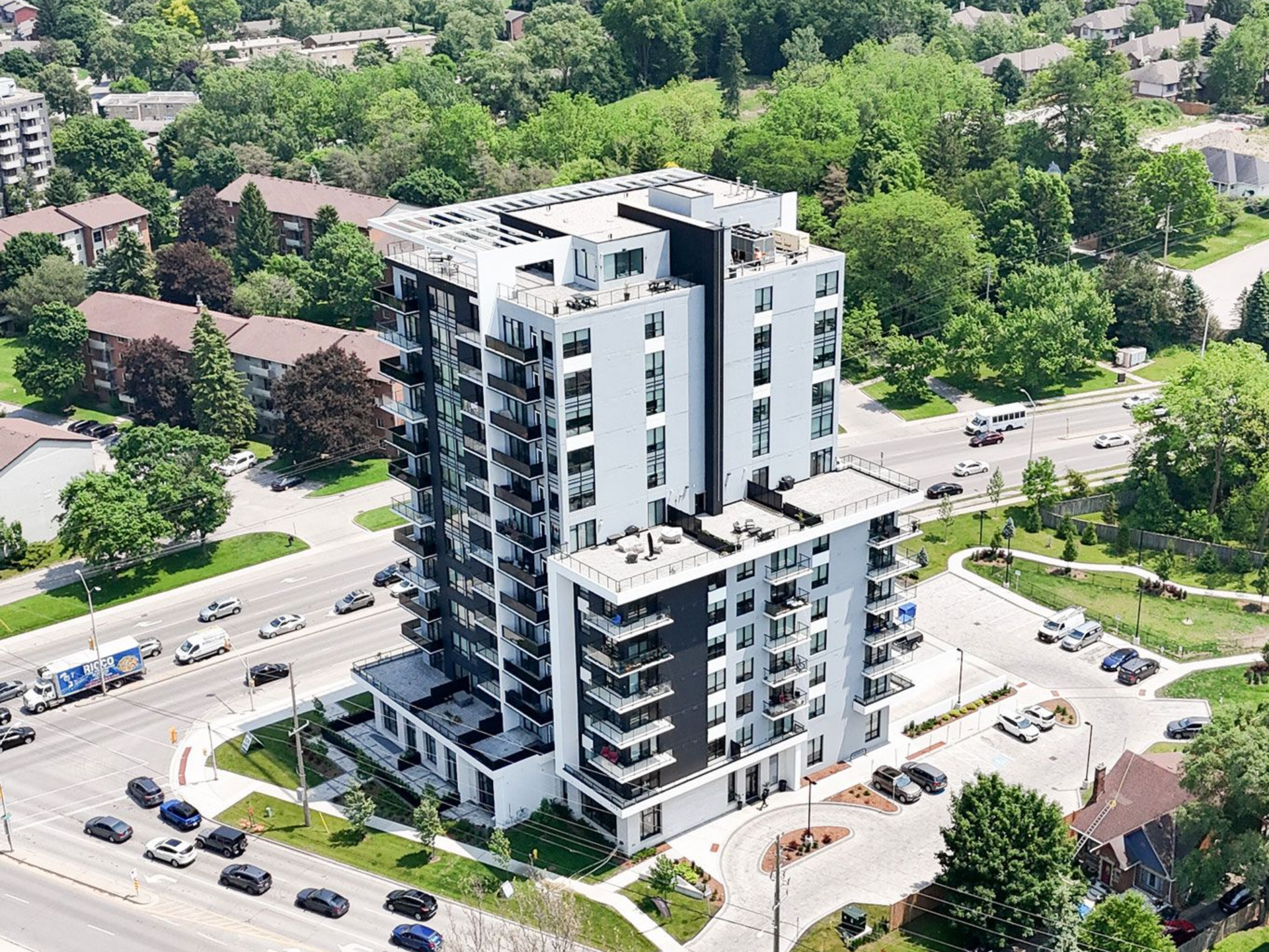 Modern high-rise apartment building, white with black accents, surrounded by greenery and roads in London Ontario