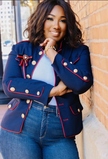 Woman in blue jacket and jeans, leaning against a brick wall, smiling.