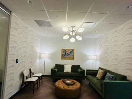 Reception area with wooden bench, leather sofa, chairs, plants, and a dark wooden door.