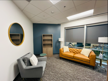 Waiting room with tan leather sofa, two chairs on either side, plants, and wall art.