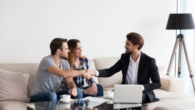 property-manager-sitting-on-a-couch-with-a-couple-shaking-hands