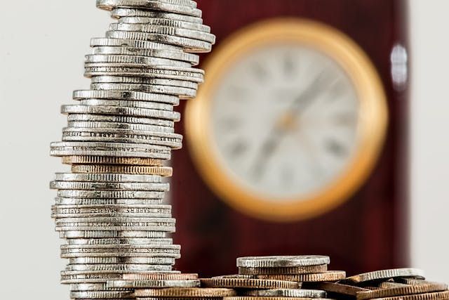  large-stack-of-coins-in-front-of-an-out-of-focus-clock