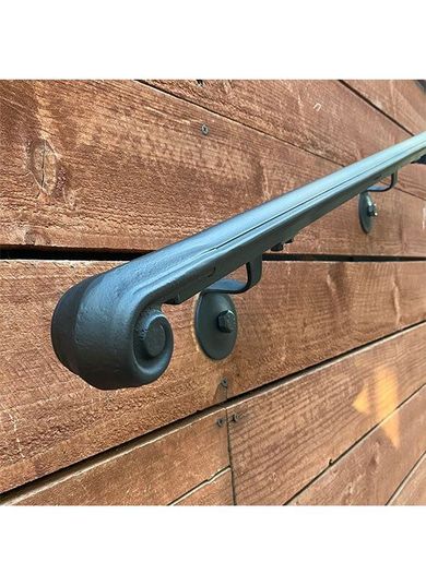 A wrought iron handrail is attached to a wooden wall.